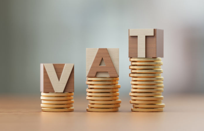Cube Blocks And Coins Forming VAT Text Over Defocused Background Pilot scheme introduces VAT in lieu of business tax