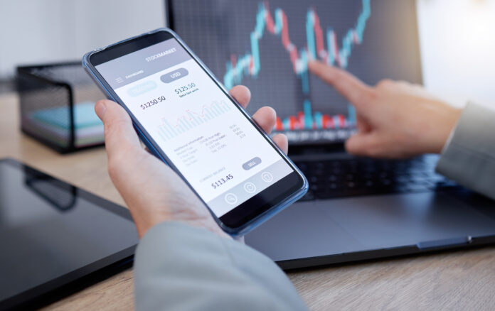 Hands, phone and laptop in trading for cryptocurrency, NFT or blockchain monitoring candle stick chart of investment. Hand of trader or broker with smartphone app on stock market for ecommerce Deal highlights March 2023
